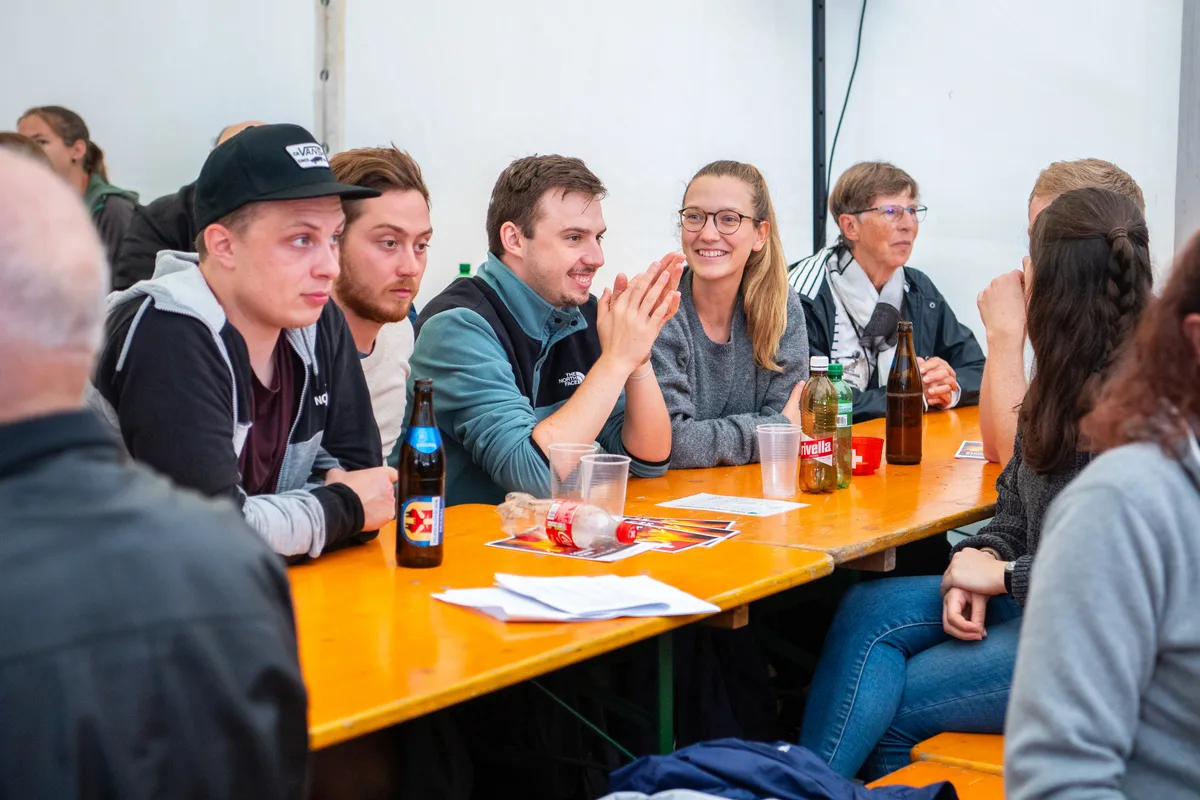 Junge Männer und Frauen sitzen am Tisch.